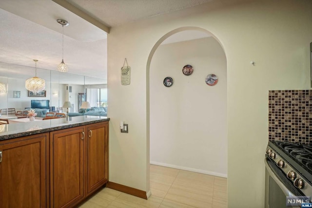 kitchen featuring an inviting chandelier, decorative backsplash, a textured ceiling, decorative light fixtures, and stainless steel range oven