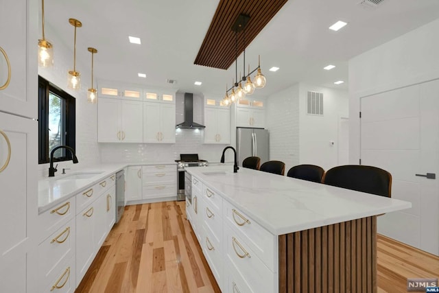 kitchen with a center island with sink, white cabinets, wall chimney range hood, sink, and stainless steel appliances