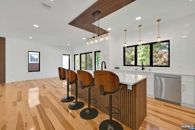 kitchen featuring white cabinetry, stainless steel dishwasher, decorative light fixtures, and light hardwood / wood-style floors