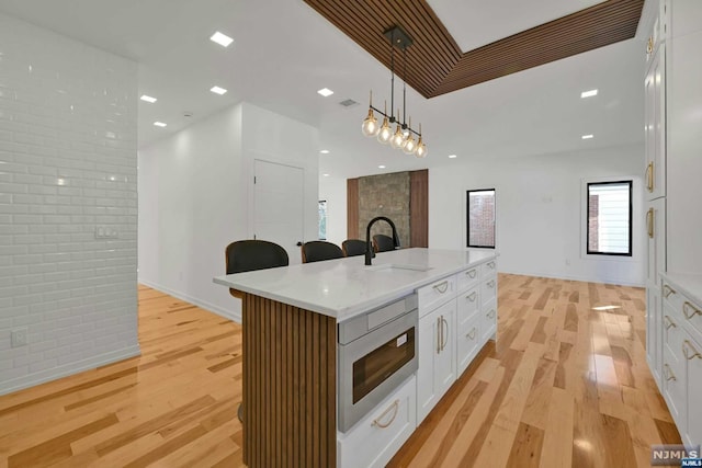 kitchen with white cabinets, decorative light fixtures, a center island with sink, and light hardwood / wood-style floors