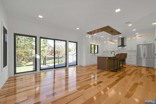 kitchen featuring stainless steel fridge, plenty of natural light, hanging light fixtures, and wall chimney range hood