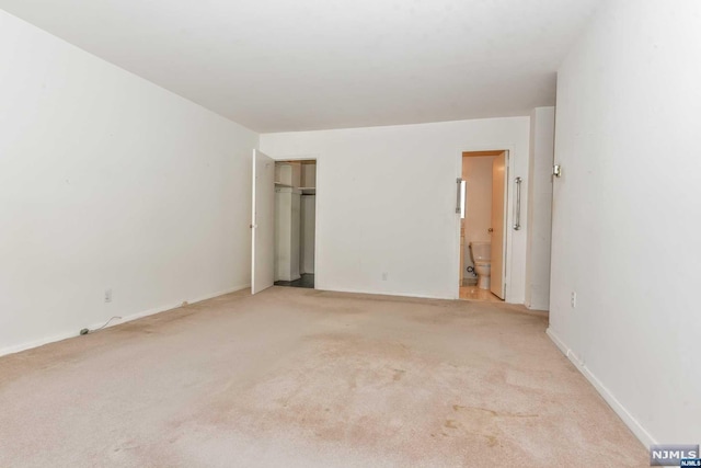 unfurnished bedroom with ensuite bathroom, light carpet, and a closet