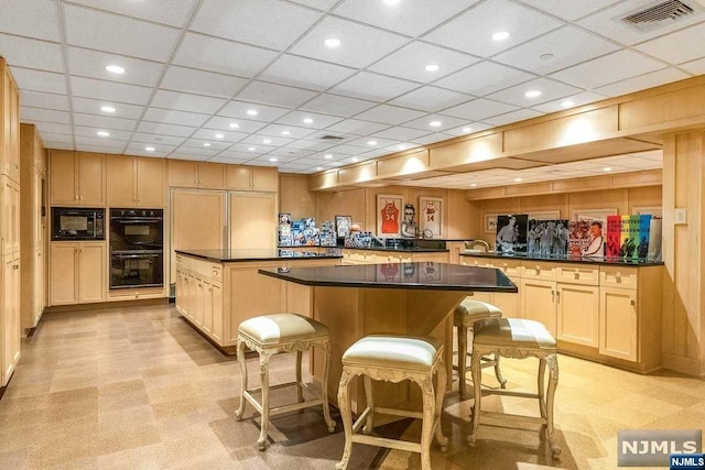 kitchen with a kitchen breakfast bar, kitchen peninsula, a spacious island, light brown cabinetry, and black appliances