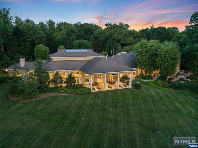 back house at dusk with a lawn, a patio, and solar panels