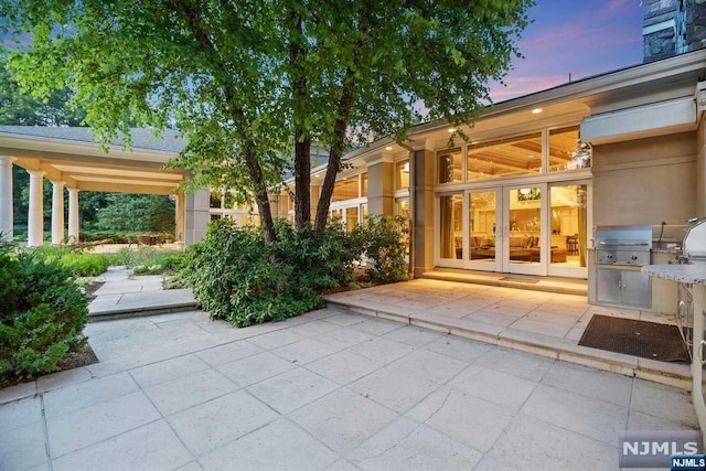 patio terrace at dusk featuring a grill, french doors, and an outdoor kitchen