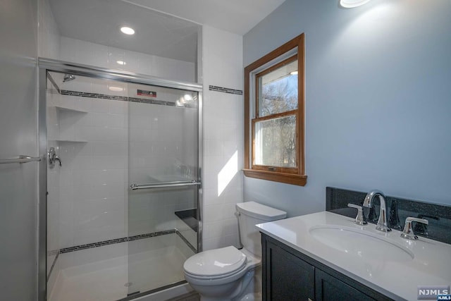 bathroom featuring vanity, a shower with door, and toilet