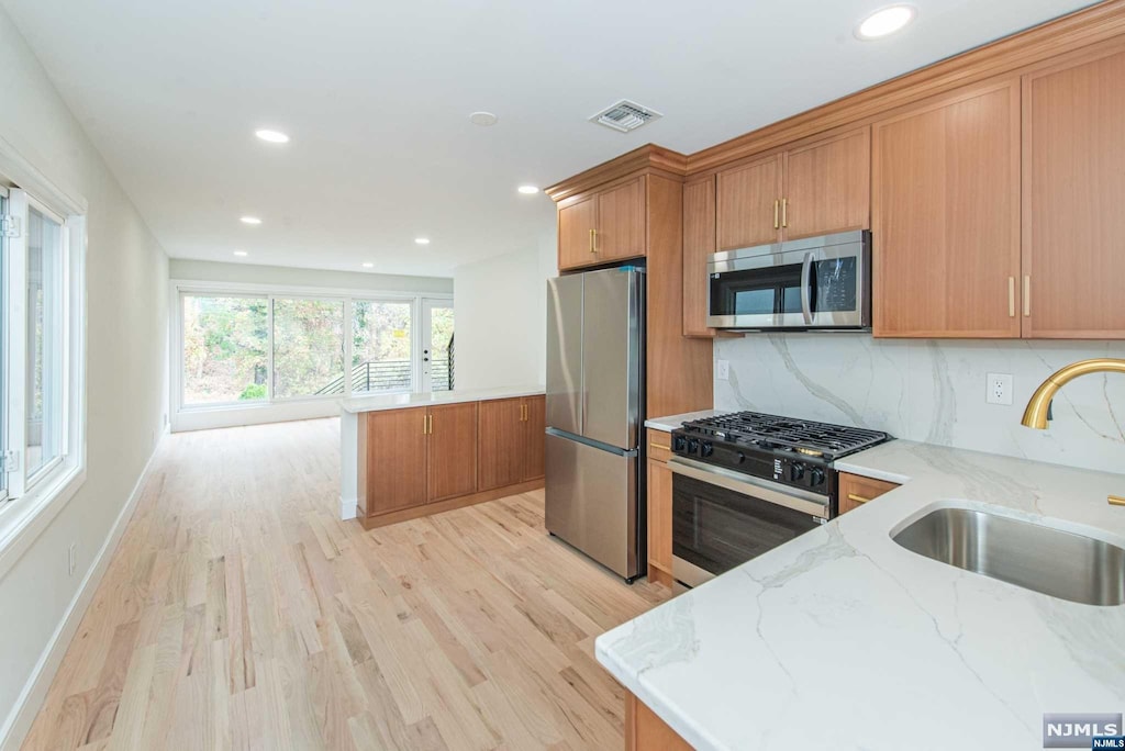 kitchen featuring sink, light hardwood / wood-style flooring, decorative backsplash, appliances with stainless steel finishes, and light stone counters