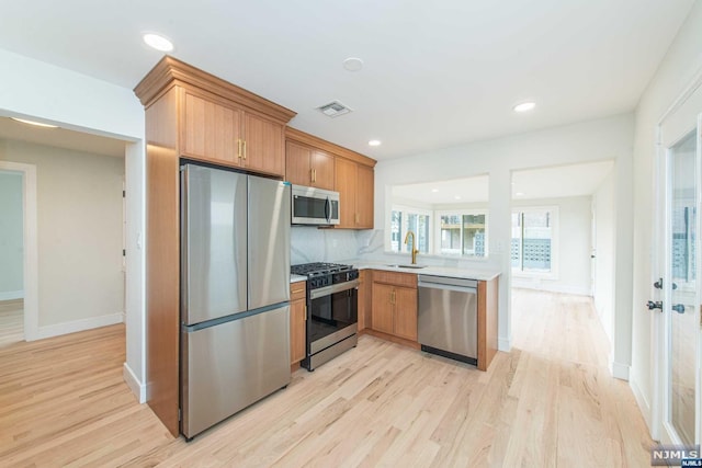 kitchen featuring sink, stainless steel appliances, backsplash, kitchen peninsula, and light hardwood / wood-style floors