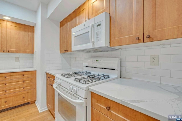 kitchen with white appliances, light stone counters, light hardwood / wood-style flooring, and backsplash