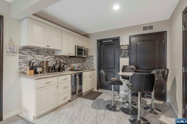 bar featuring light stone countertops, backsplash, and beverage cooler