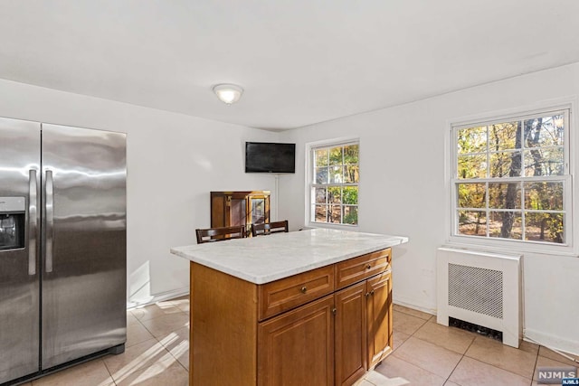 kitchen with radiator, a kitchen island, light tile patterned flooring, and stainless steel refrigerator with ice dispenser