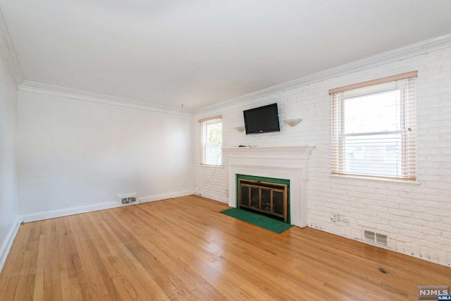 unfurnished living room with hardwood / wood-style floors, crown molding, a healthy amount of sunlight, and brick wall