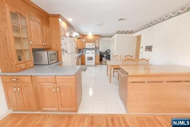 kitchen with kitchen peninsula, light tile patterned flooring, white appliances, and ornamental molding