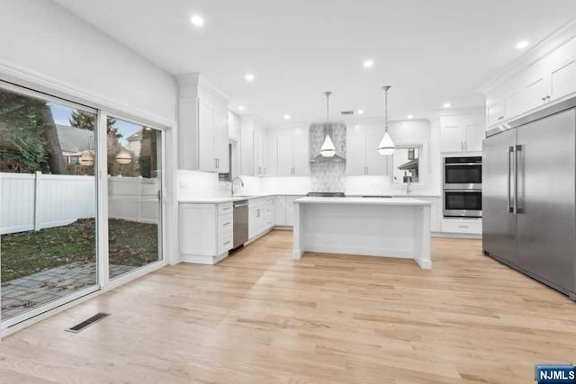 kitchen with white cabinetry, wall chimney exhaust hood, light hardwood / wood-style flooring, pendant lighting, and appliances with stainless steel finishes