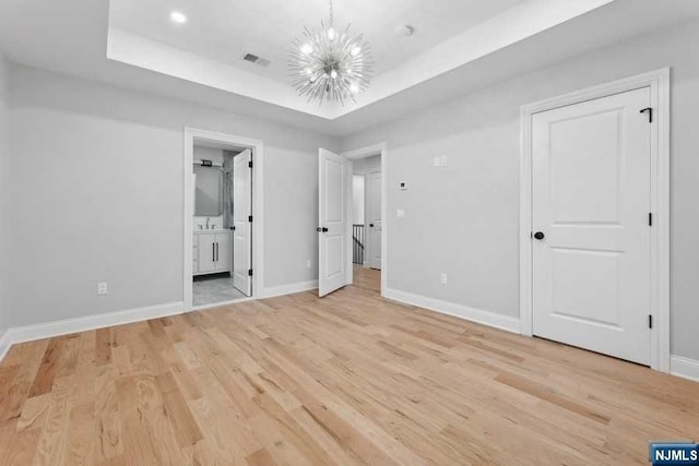 unfurnished bedroom with ensuite bath, sink, a chandelier, light hardwood / wood-style floors, and a tray ceiling