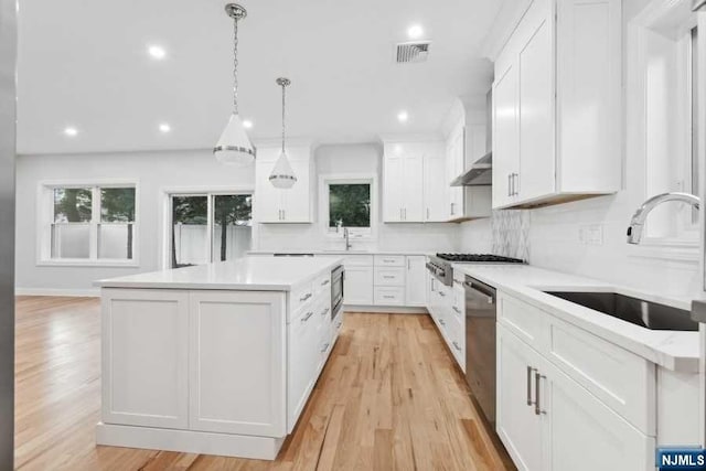 kitchen with light wood-type flooring, sink, decorative light fixtures, white cabinets, and a center island