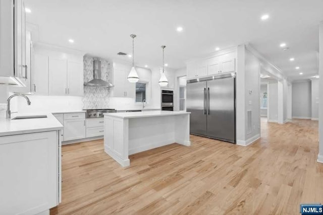 kitchen with wall chimney exhaust hood, stainless steel appliances, sink, white cabinets, and a center island