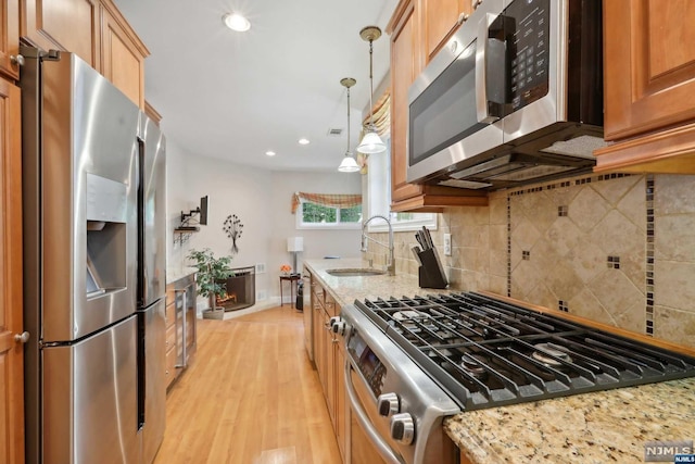 kitchen featuring light stone countertops, appliances with stainless steel finishes, sink, pendant lighting, and light hardwood / wood-style floors