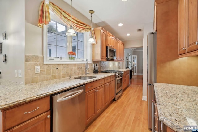 kitchen featuring sink, hanging light fixtures, stainless steel appliances, light stone counters, and light hardwood / wood-style flooring