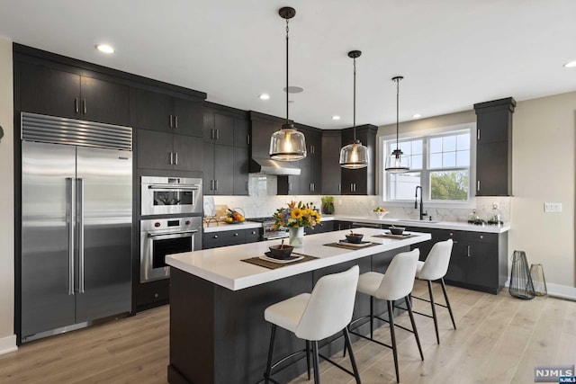 kitchen featuring decorative light fixtures, a kitchen island, stainless steel appliances, and light hardwood / wood-style flooring