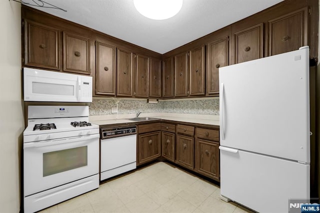 kitchen with tasteful backsplash, sink, dark brown cabinetry, and white appliances