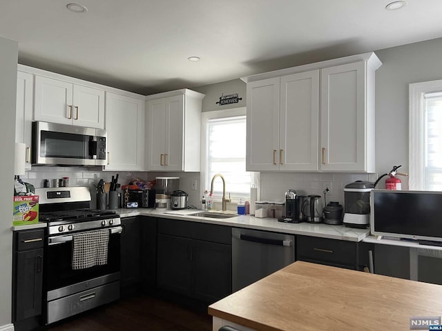 kitchen with sink, dark wood-type flooring, stainless steel appliances, backsplash, and white cabinets