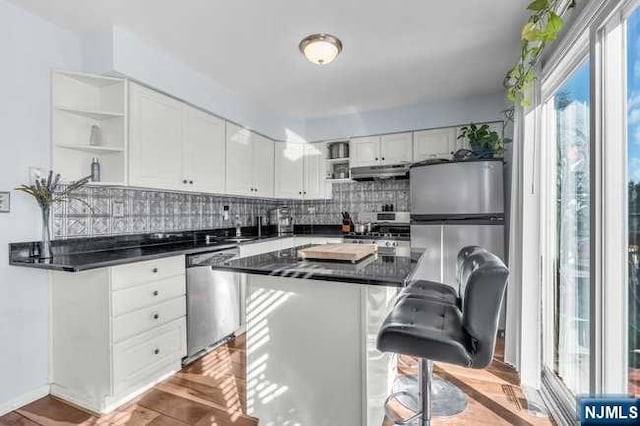 kitchen featuring a center island, backsplash, a kitchen bar, white cabinets, and appliances with stainless steel finishes