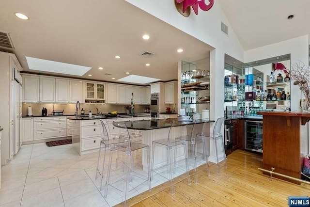 kitchen with kitchen peninsula, a kitchen bar, white cabinetry, light hardwood / wood-style floors, and wine cooler