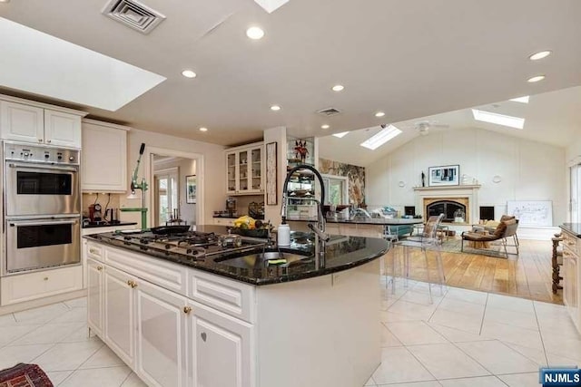 kitchen with lofted ceiling with skylight, a center island with sink, white cabinets, dark stone countertops, and stainless steel appliances