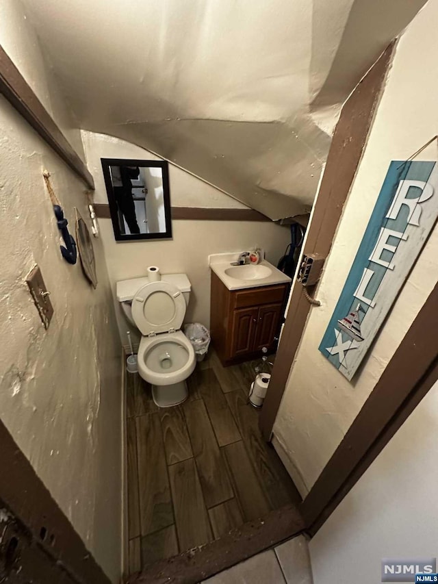 bathroom featuring vanity, toilet, wood-type flooring, and lofted ceiling