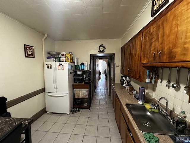 kitchen featuring sink, tasteful backsplash, white refrigerator, crown molding, and light tile patterned floors