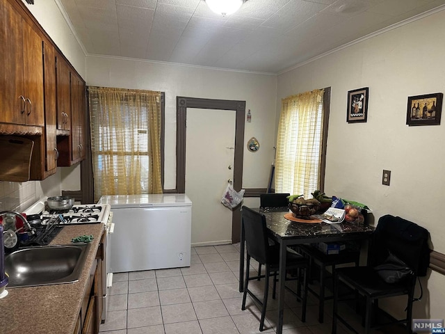 kitchen featuring sink, crown molding, fridge, light tile patterned floors, and white gas range oven