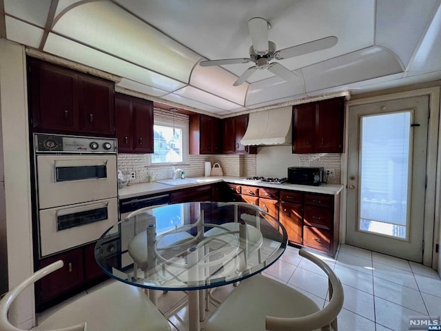 kitchen featuring decorative backsplash, premium range hood, double oven, sink, and light tile patterned floors