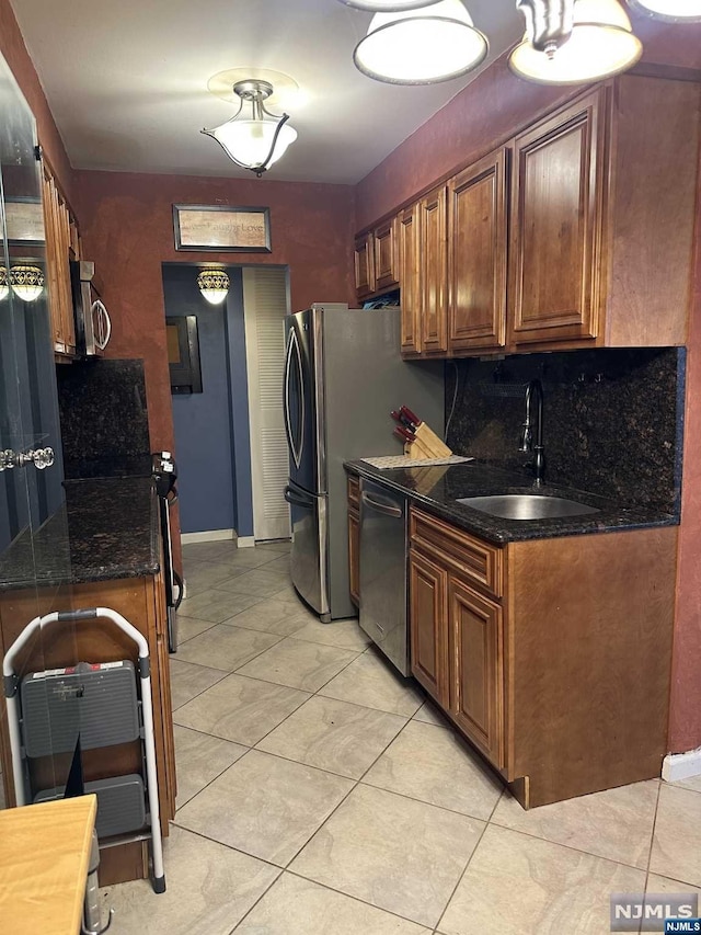 kitchen with appliances with stainless steel finishes, tasteful backsplash, sink, light tile patterned floors, and dark stone countertops