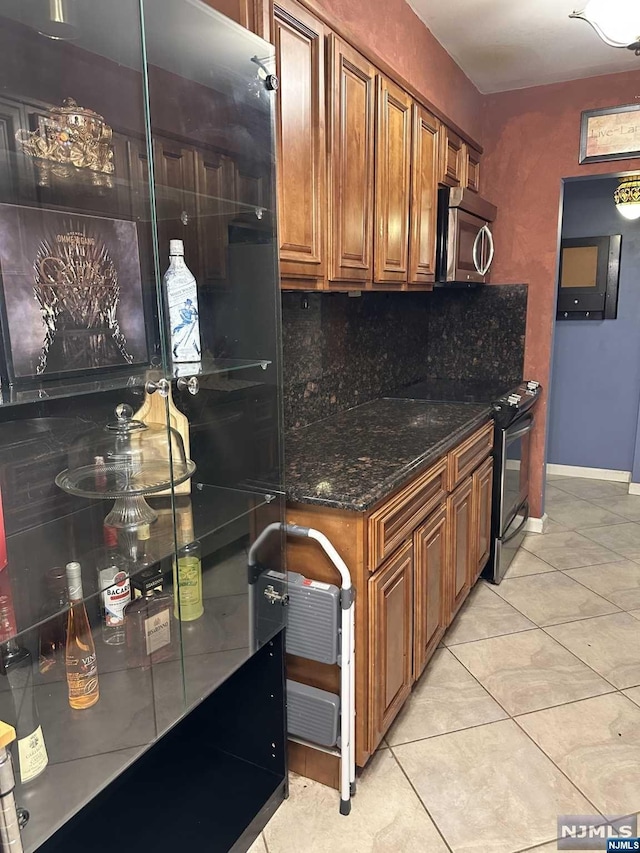 kitchen with light tile patterned floors, stainless steel appliances, dark stone counters, and tasteful backsplash