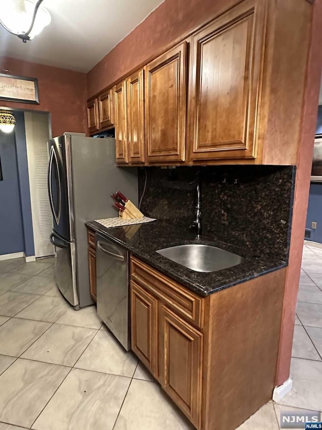 kitchen with sink, dark stone counters, decorative backsplash, light tile patterned floors, and appliances with stainless steel finishes