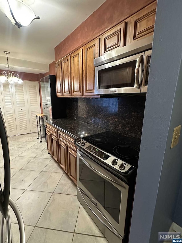 kitchen with appliances with stainless steel finishes, backsplash, a chandelier, hanging light fixtures, and light tile patterned flooring