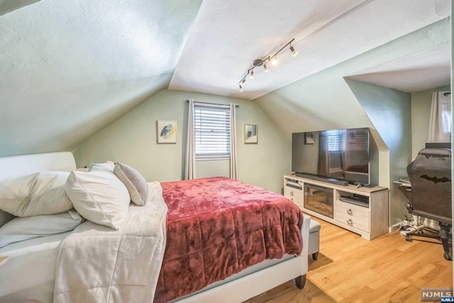 bedroom featuring a textured ceiling, light hardwood / wood-style flooring, track lighting, and lofted ceiling