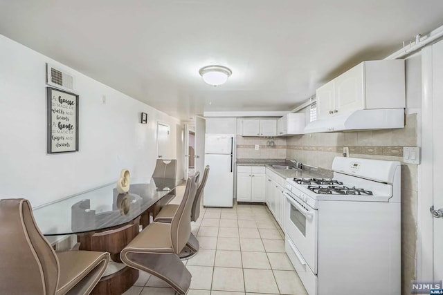 kitchen featuring white appliances, backsplash, sink, light tile patterned floors, and white cabinetry