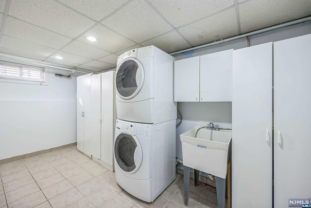 washroom with stacked washer and dryer, light tile patterned floors, cabinets, and sink