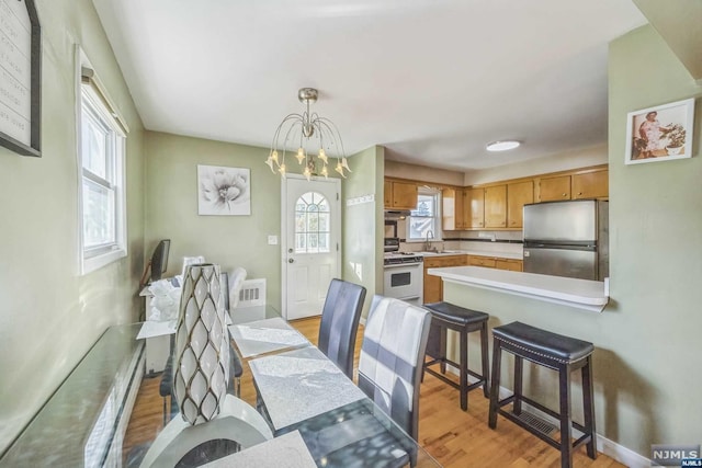 dining area with a healthy amount of sunlight, light wood-type flooring, sink, and a chandelier