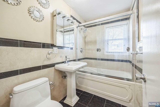 bathroom with tile patterned floors, enclosed tub / shower combo, tile walls, and toilet