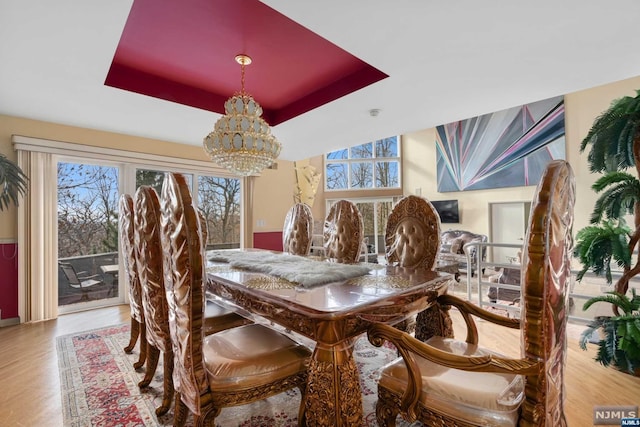 dining area with hardwood / wood-style flooring, plenty of natural light, an inviting chandelier, and a tray ceiling