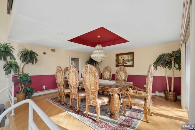 dining room with a notable chandelier, light hardwood / wood-style floors, a tray ceiling, and a baseboard heating unit