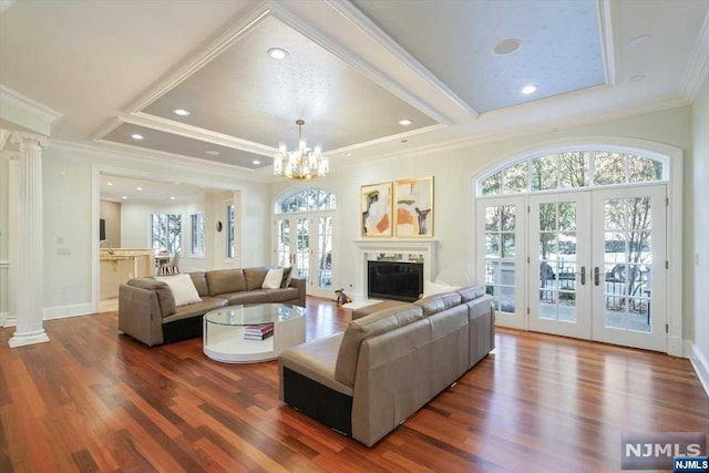 living room with ornate columns, french doors, a notable chandelier, hardwood / wood-style floors, and ornamental molding