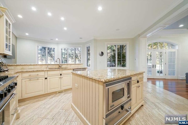 kitchen with sink, a center island, stainless steel appliances, light stone counters, and light wood-type flooring