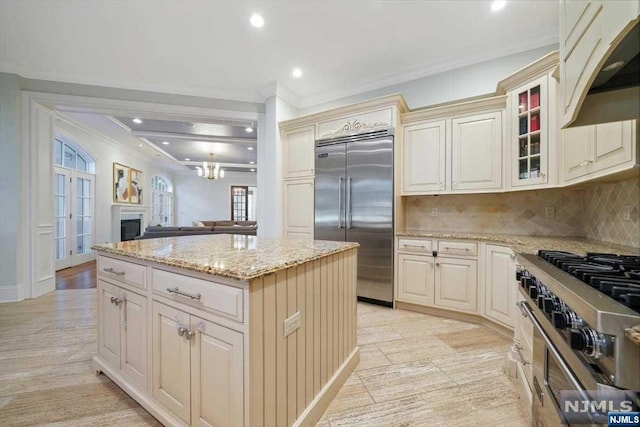 kitchen with decorative backsplash, light stone counters, cream cabinets, high quality appliances, and a kitchen island