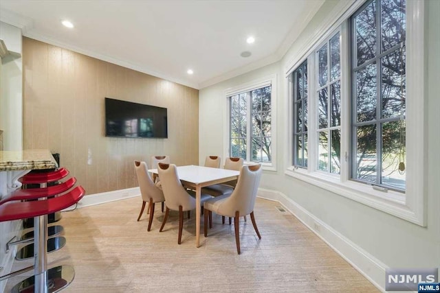 dining space featuring ornamental molding, wooden walls, and light hardwood / wood-style flooring