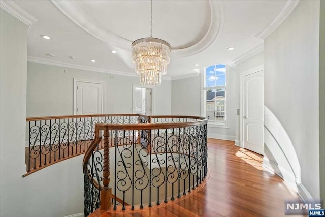 corridor featuring wood-type flooring, crown molding, a tray ceiling, and an inviting chandelier