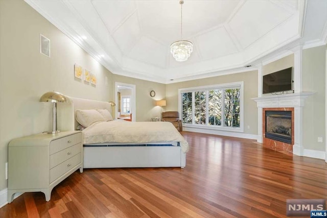 bedroom with a raised ceiling, hardwood / wood-style floors, a chandelier, a tiled fireplace, and ornamental molding